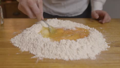 Chef-mixing-egg-yolks-with-the-pasta-dough-with-fork