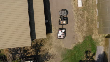 Farmer's-ATV-transporting-trailer-full-of-white-boxes-with-fresh-produce,-aerial-top-down-shot