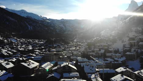 sunshine-on-snow-covered-houses-of-Zermatt-valley-winter-resort,-aerial-shot