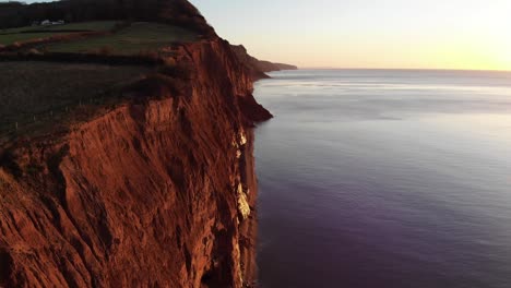 Aerial-Along-Sidmouth-Coastline-Cliffs-Bathed-In-Golden-Sunrise-Light-In-The-Morning