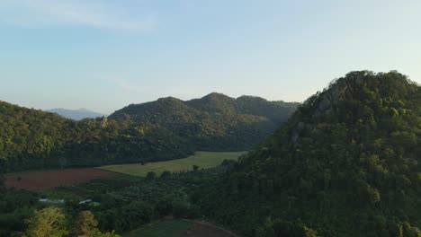 Luftaufnahmen-In-Richtung-Eines-Tals-Mit-Bauernhöfen-Und-Den-Hügeln,-Die-Es-Umgeben,-Mit-Schönem-Blauem-Himmel-In-Pakchong,-Khao-Yai,-Thailand