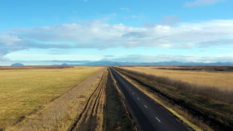 Empty-two-way-road,-yellow-scenic-asphalt-route-landscape-in-Iceland,-pull-back-aerial-drone-shot
