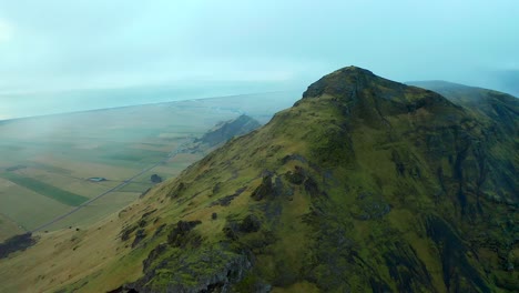 Flyover-Volcanic-mountains-surrounded-by-fog,-mountain-range-towards-Skogafoss-waterfall,-Iceland