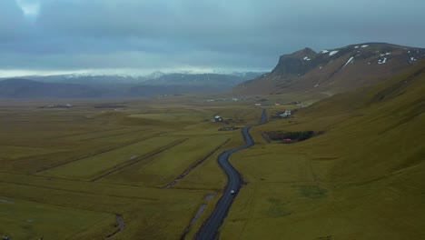 Aerial-view-of-a-car-traveling-in-a-country-road-through-a-moody-valley,-Iceland