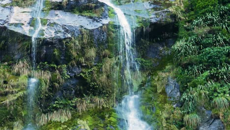 Wide-shot-of-cascade-waterfall-flowing-downhill-vegetated-mountains---Milford-Track-in-New-Zealand
