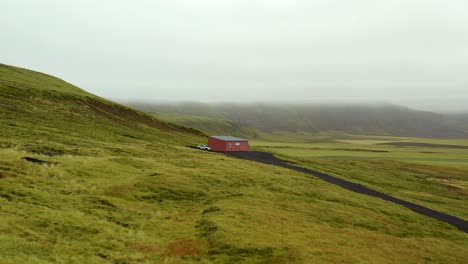 Jib-up-shot-of-a-cabin-in-the-hillside-of-a-green-mossland-in-Iceland,-foggy
