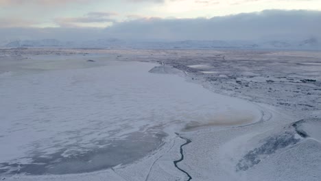 Aerial-drone-shot-of-snow-covered-and-frozen-My-vatn-Lake-during-cloudy-and-sunny-day-in-Iceland---In-foreground-volcanic-tuff-ring-volcano