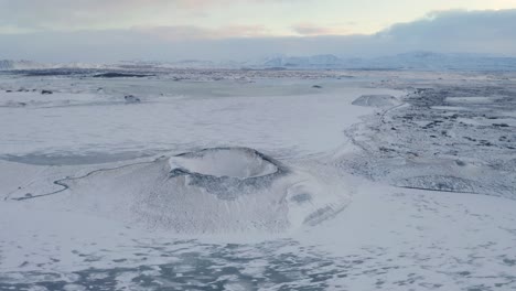 Luftbahnaufnahme-Des-Schneebedeckten-Vulkankraters-Und-Des-Gefrorenen-Sees-My-Vatn-Im-Hintergrund-Während-Des-Wintertages-In-Island