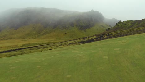 Flyover-Icelandic-green-fields-with-mountains-Background,-Mystical-fog-Scenery