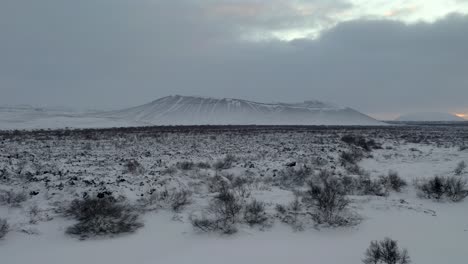Aerial-panorama-shot-of-famous-Hverfjall-Crater-during-snowy-winter-day-with-dense-clouds-at-sky-during-sunset-at-horizon