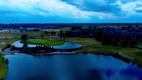 golf-course-next-to-detached-large-home-community-with-man-made-greens-pond-well-designed-gardens-water-falls-aerial-flyover-summer-day-reflection-on-the-water-surface-clouds-showing-private-pathway