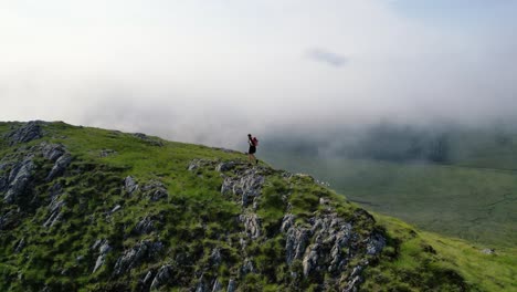 Male-with-orange-backpack-running-over-the-green-hills-in-the-Scottish-Wilderness-on-a-low-hanging-misty-day