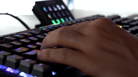 Mano-De-Un-Jugador-Escribiendo-Y-Usando-Un-Teclado-Colorido,-Cerca-De-Una-Persona-Irreconocible-Jugando-Videojuegos-De-Computadora