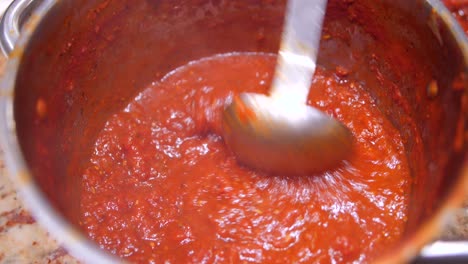 Close-up-view-of-homemede-tomato-sauce-boiling-in-a-pan,-being-stirred-with-a-spoon