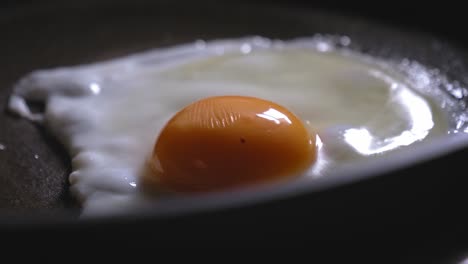 A-closeup-abstract-shot-of-a-spluttering-sunny-side-up-egg-cooking-in-a-hot-frying-pan,-the-fried-egg-topped-with-ham-and-grated-cheese-creating-a-tasty-filling-with-seasoning-for-a-gourmet-sandwich