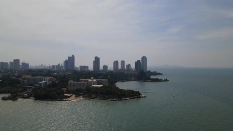 Reverse-aerial-footage-of-the-beachfront-in-Pattaya-and-the-Sanctuary-of-Truth-with-some-buildings,-Chonburi,-Thailand