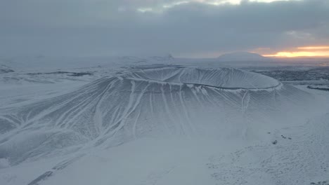 Aerial-drone-shot-of-snowy-Hverfjall-Crater-during-mystical-sunset-in-background---Iceland,Europe