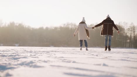 Loving-couple-ice-skating-in-an-outdoor-winter-landscape-while-holding-hands,-back-view-of-romantic-snowy-scene