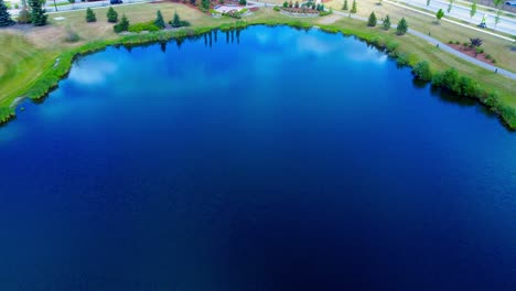 golf-course-aerial-flyover-reflective-birds-top-eye-view-over-garden-waterfall-tiered-from-pond-to-pond-closeup-shore-pathway-next-to-roadway-in-the-Southside-of-Edmonton-Alberta-Canada