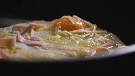 Seasoning-savoury-ham-egg-with-salt-peeper-and-paprika-in-frying-pan-closeup