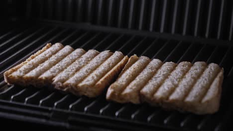 A-close-up-shot-of-the-lid-of-a-sandwich-press-being-opened-to-reveal-two-slices-of-freshly-toasted-brown-bread-on-a-steaming-hot-grill