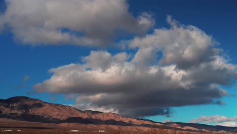 Vehicular-traffic-moving-along-the-highway-at-the-base-of-the-Mojave-Desert-mountains-with-a-cloudscape-overhead---time-lapse