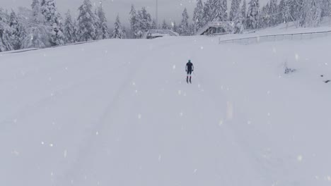 Training-cross-country-skiing-during-snowfall,-aerial-back-shot