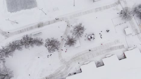 Kids-enjoy-white-winter-day-in-kindergarten-yard,-aerial-top-down-ascend-shot