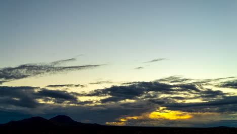 Amanecer-Dorado-Sobre-Las-Llanuras-Del-Desierto-De-Mojave-Con-Montañas-En-Silueta-Mientras-El-Paisaje-De-Nubes-Se-Vuelve-Naranja---Lapso-De-Tiempo-De-Gran-Angular