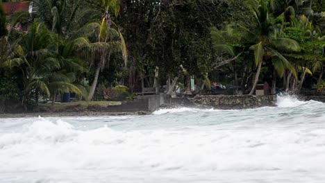 Big-long-waves-breaking-ashore-and-splashing-onto-the-rocks-in-front-of-tropical-palm-forest