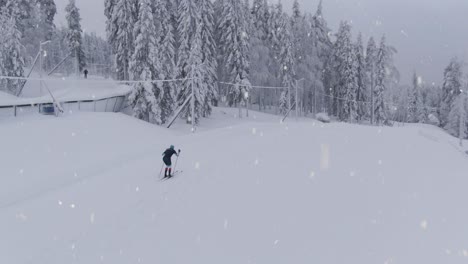 Athlete-preparing-for-winter-Olympics-in-cross-country-skiing-during-snowfall,-aerial-drone-shot