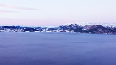 Volando-Sobre-El-Mar-En-Calma-Con-Panorama-De-Montaña-Nevada-En-Invierno-En-Noruega