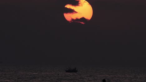 Orange-Sunset-With-Cloud-Cover-Slow-Zoom-Out-Reveal-Of-Silhouette-Of-Boat-In-Ocean
