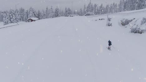 People-training-cross-country-skiing-during-snowfall,-aerial-follow-up-shot