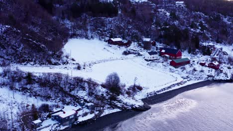 Aerial-View-Of-Snowy-Hillside-Cabins-At-Winter-With-Calm-Sea-IN-Norway