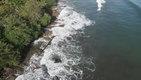 Waves-landing-on-island-with-green-trees-during-high-tide
