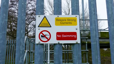 Beware-strong-current-and-no-swimming-sign-on-a-barrier-metal-bar-wall