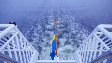 Swedish-Flag-On-The-Back-Of-A-Sailing-Boat-With-Backwash-In-The-Background