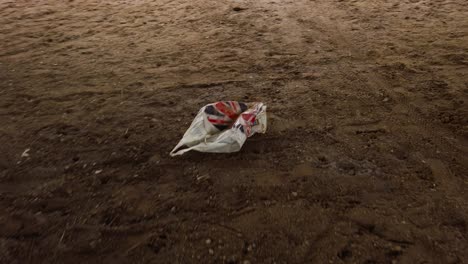 Carrier-plastic-bag-on-muddy-sandy-soil-ground,-environment-pollution-concept---handheld-shot