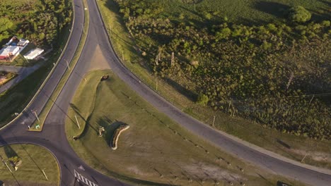 Aerial-high-angle-top-down-of-Motorbike-turning-on-curvy-exit-road-during-sunny-day-in-rural-area-of-Uruguay