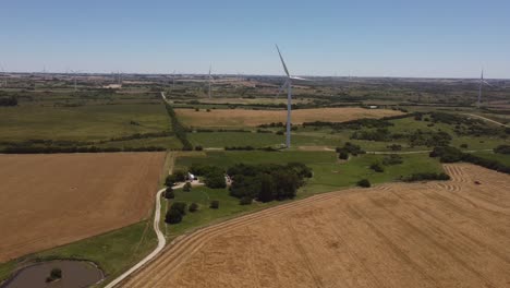 Aerial-backwards-flight-showing-spinning-Wind-Turbine-producing-green-energy-surrounded-by-colorful-farmland-fields-in-South-America-during-beautiful-sunny-day
