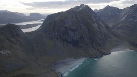 Aerial-view-overlooking-the-Kvalvika-and-Vestervika-beaches,-shadowed-by-steep-mountains-of-Lofoten,-Norway---pan,-drone-shot