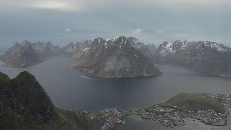 Aerial-view-overlooking-the-Reine-town,-in-cloudy-Lofoten,-Norway---reverse,-drone-shot