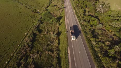 Aerial-tracking-shot-of-industrial-truck-driving-on-rural-asphalt-road-in-Uruguay-during-sunset-time