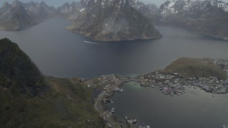 Aerial-view-overlooking-the-Reine-village-and-mountains-surrounding-it,-in-cloudy-Lofoten,-Norway---tilt,-drone-shot