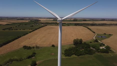 Aerial-close-up-shot-of-rotating-wind-turbine-and-agricultural-fields-in-backdrop