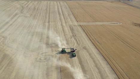 Aerial-pullback,-combine-harvester-on-wheat-field-harvesting-grain-into-tractor-bed