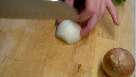 Female-Hands-Cutting-a-Onion-on-a-Wooden-Cutting-Board
