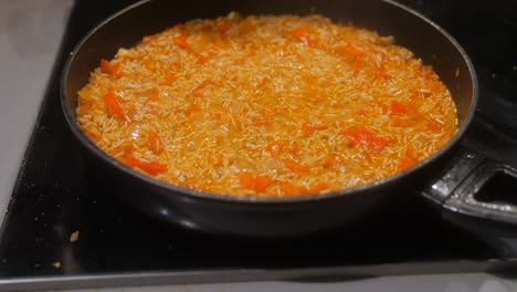 Close-up-shot-of-the-rice-cooking-in-a-pan-with-vegetables-on-the-stove-serving-hot