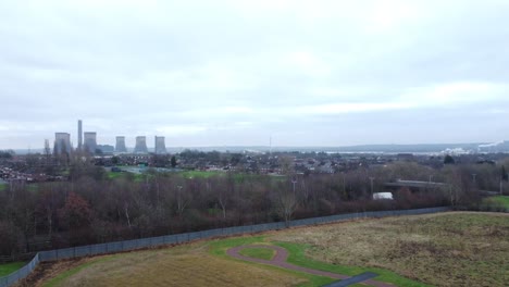Rising-aerial-view-across-rural-countryside-park-with-power-station-smoke-stacks-on-distant-horizon-dolly-left